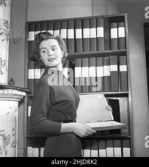 Office fille dans le 1950s.Une femme est photographiée devant une étagère avec des classeurs et elle a un sorti qui contient ce qu'elle recherchait.Elle est joliment habillée et donne une impression sérieuse.Suède 1954.photo Kristoffersson BO24-12 Banque D'Images