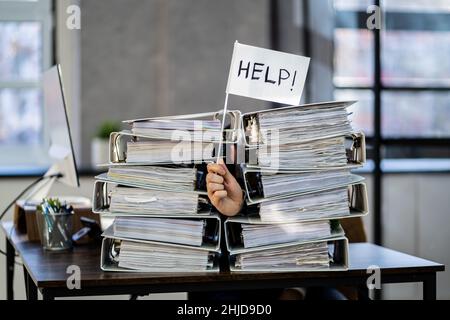 Sad Men in Office with Tax Workload and Paper Files Holding Help Flag Banque D'Images