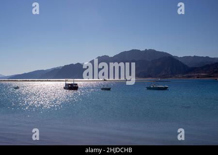 Le soleil se reflétant sur un magnifique lagon bleu à Dahab, en Égypte. Bateaux dans l'eau avec les montagnes derrière Banque D'Images