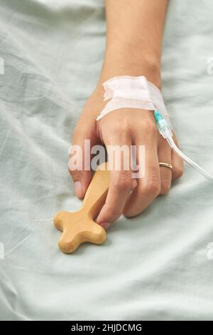 Un cliché vertical de la main d'un patient relié à un goutte-à-goutte IV tenant une croix en bois Banque D'Images