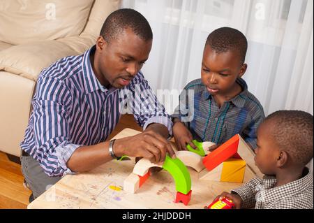 un garçon de 2 ans regarde le père et le frère de 4 ans, en attendant qu'ils construisent un tunnel pour le camion qu'il tient Banque D'Images
