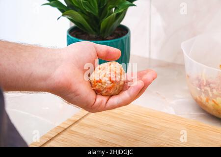 Un homme sculpte des petits pains de chou paresseux à partir de viande hachée, de chou, de riz.L'homme forme des boules de viande. Banque D'Images