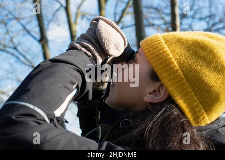 Personne avec un chapeau et des gants d'observation des oiseaux lors d'une journée d'hiver ensoleillée dans la nature Banque D'Images