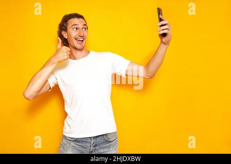 l'homme excité prend le selfie sur son téléphone, donne le pouce vers le haut signe communique bien via smartphone vidéo Banque D'Images