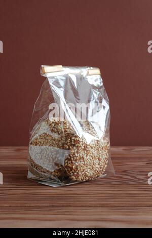 Biscuits aux flocons d'avoine avec graines de sésame dans un sac transparent sur une table en bois contre un mur brun.Gros plan. Banque D'Images