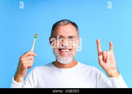 homme montrant une brosse à dents multicolore arc-en-ciel dans un studio bleu Banque D'Images