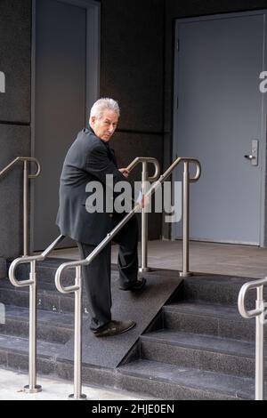 Homme d'affaires marchant sur une très étroite rampe pour handicapés vers un immeuble de bureaux Banque D'Images