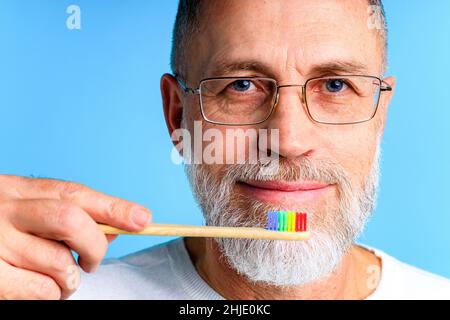 homme montrant une brosse à dents multicolore arc-en-ciel dans un studio bleu Banque D'Images