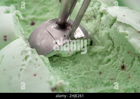 Rafraîchissement délicieux et soin rafraîchissant de l'été avec une pelle en métal qui ramasse une boule verte de pistache lisse ou de crème glacée à la menthe Banque D'Images