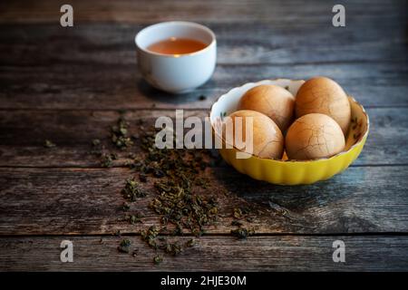 Des œufs de thé épicés en marbre chinois dur sur une table rustique en bois avec des feuilles de thé et une tasse de thé chinois en arrière-plan. Banque D'Images