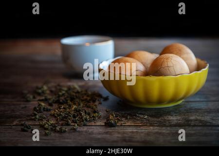 Des œufs de thé épicés en marbre chinois dur sur une table rustique en bois avec des feuilles de thé et une tasse de thé chinois en arrière-plan. Banque D'Images