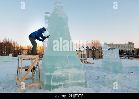 Le sculpteur coupe une figure de glace d'un bloc de glace avec un burin pour NOËL étant sur un échafaudage en bois Banque D'Images