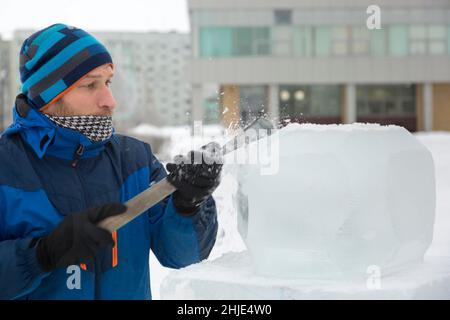 Un sculpteur sculpta une boule de glace ronde sur un bloc de glace avec un burin. Banque D'Images