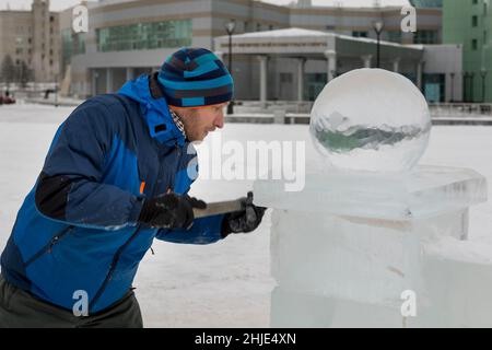 Un sculpteur sculpta une boule de glace ronde sur un bloc de glace avec un burin. Banque D'Images