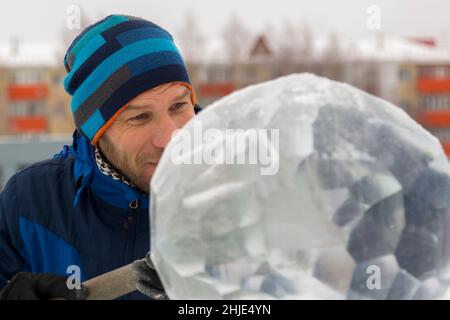 Un sculpteur sculpta une boule de glace ronde sur un bloc de glace avec un burin. Banque D'Images