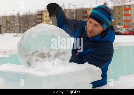 Un sculpteur sculpta une boule de glace ronde sur un bloc de glace avec un burin. Banque D'Images