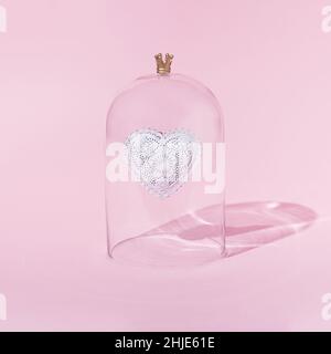 Coeur dans une cloche de verre sur fond rose.Concept minimal de la Saint-Valentin.Carré avec espace de copie.Présentation isométrique. Banque D'Images