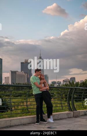 Charmant couple mixte debout sur le pont dans le parc en métropole et en cuddling.Concept d'amour et de bonheur.Gratte-ciel en arrière-plan Banque D'Images