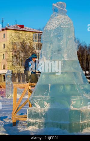 Le sculpteur coupe une figure de glace d'un bloc de glace avec un burin pour NOËL étant sur un échafaudage en bois Banque D'Images