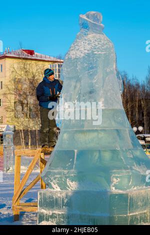 Le sculpteur coupe une figure de glace d'un bloc de glace avec un burin pour NOËL étant sur un échafaudage en bois Banque D'Images