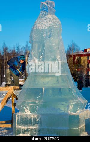 Le sculpteur coupe une figure de glace d'un bloc de glace avec un burin pour NOËL étant sur un échafaudage en bois Banque D'Images