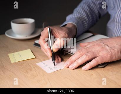 L'homme d'affaires écrit des notes de mémo ou un rappel sur l'autocollant au bureau. Banque D'Images