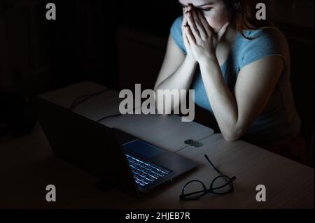 une femme fait des heures supplémentaires.Un étudiant étudiant étudiant étudiant à un ordinateur portable la nuit dans l'obscurité.La jeune fille s'inquiète des problèmes au travail et tient ses mains sur son visage. Banque D'Images