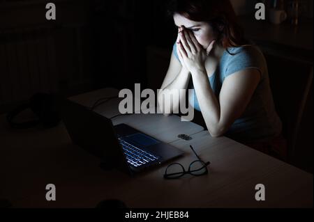 une femme fait des heures supplémentaires.Un étudiant étudiant étudiant étudiant à un ordinateur portable la nuit dans l'obscurité.La jeune fille s'inquiète des problèmes au travail et tient ses mains sur son visage. Banque D'Images