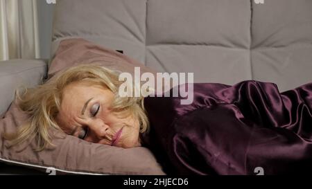 Une femme âgée s'étend sur un canapé et s'endort fatiguée après le travail Banque D'Images