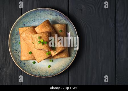 Crêpes fines farcies à l'aneth frais et à l'oignon sur fond noir.Vue de dessus, espace de copie.Petits pains à crêpes.Crêpes russes traditionnelles pour Maslenits Banque D'Images