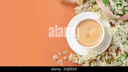 Tasse à cappuccino avec fleurs et ruban sur fond orange.Vue de dessus, espace de copie. Banque D'Images