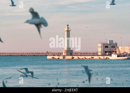 Beau phare avec mer bleue calme, mouettes et bateau de pêche garés près du quai du port Banque D'Images