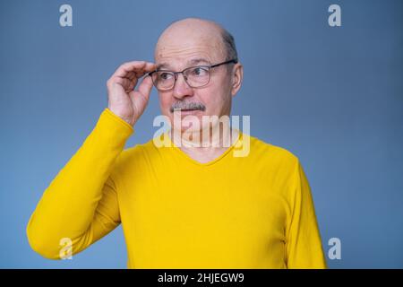 Homme hispanique senior essayant ses nouvelles lunettes.Studio tourné sur fond bleu Banque D'Images