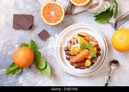 Fête du Pancake, petit déjeuner sain.Délicieuses crêpes américaines maison à la banane avec chocolat et orange rouge sur fond de pierre grise.Plat Banque D'Images