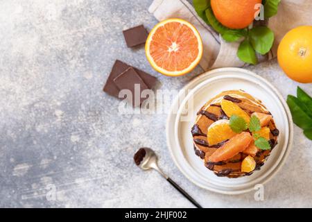 Fête du Pancake, petit déjeuner sain.Délicieuses crêpes américaines maison à la banane avec chocolat et orange rouge sur fond de pierre grise.Plat Banque D'Images