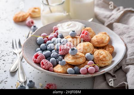 Délicieux poffertjes aux bleuets et framboises congelés.Petit déjeuner avec mini crêpes et baies glacées. Banque D'Images