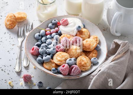 Mini crêpes faites maison avec myrtilles et framboises congelées.Petit déjeuner avec mini crêpes et baies glacées. Banque D'Images