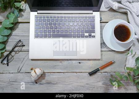 ordinateur portable clavier, tasse à café, verres et stylo sur une table rustique en bois gris avec des branches vertes et un foulard blanc, affaires dans le bureau à la maison Banque D'Images