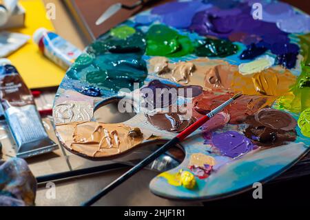 Palette avec peintures à l'huile et un pinceau.Processus de peinture, atelier d'art.Différentes couleurs de peinture appliquées pour le mélange. Banque D'Images