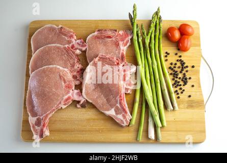 Une planche en bois avec des côtelettes de porc, des asperges et des tomates cerises Banque D'Images