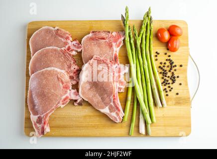 Une planche en bois avec des côtelettes de porc, des asperges et des tomates cerises Banque D'Images