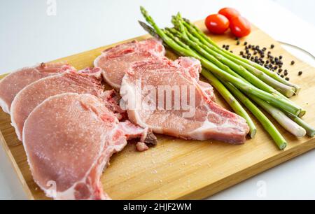 Une planche en bois avec des côtelettes de porc, des asperges et des tomates cerises Banque D'Images