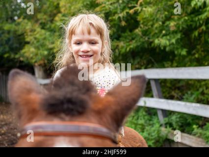 Petite fille à cheval petit poney et rire Banque D'Images