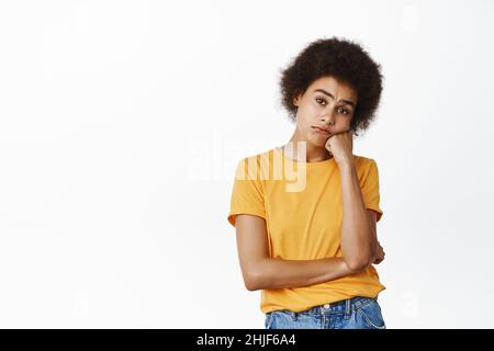 Jeune femme africaine triste qui a l'air ennuyeuse ou impopulaire, réticente face bouleversée, sombre émotion, debout sur fond blanc Banque D'Images