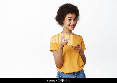 C'est vous.Souriante femme afro-américaine pointant du doigt la caméra, félicitant, choisissant la gagnante, invitant les gens à visiter le magasin, debout sur du blanc Banque D'Images