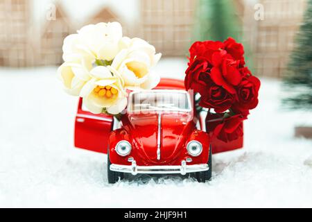 Voiture rétro rouge avec fleurs dans un paysage d'hiver.Carte postale pour la fête des mères ou la Saint-Valentin.Livraison de fleurs pour les vacances.Mise au point sélective. Banque D'Images