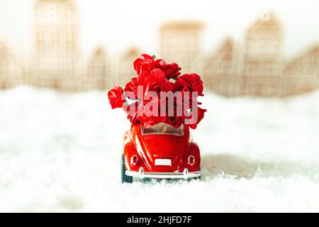 Voiture rétro rouge avec fleurs dans un paysage d'hiver.Carte postale pour la fête des mères ou la Saint-Valentin.Livraison de fleurs pour les vacances.Mise au point sélective. Banque D'Images