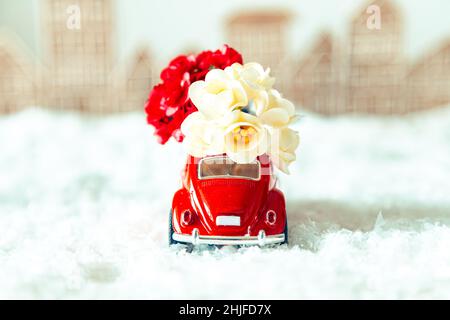 Voiture rétro rouge avec fleurs dans un paysage d'hiver.Carte postale pour la fête des mères ou la Saint-Valentin.Livraison de fleurs pour les vacances.Mise au point sélective. Banque D'Images