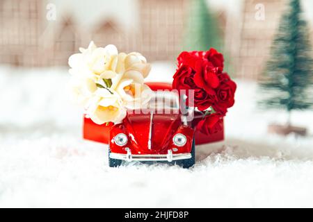 Voiture rétro rouge avec fleurs dans un paysage d'hiver.Carte postale pour la fête des mères ou la Saint-Valentin.Livraison de fleurs pour les vacances.Mise au point sélective. Banque D'Images