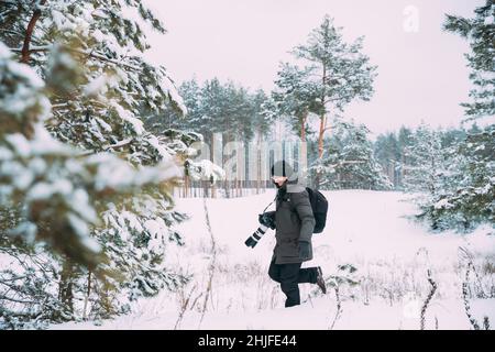 Jeune homme Backpacker avec Appareil Photo Photo Photo prise en hiver forêt enneigée. Passe-temps actif. Randonneur marchant dans la forêt de pins enneigés Banque D'Images